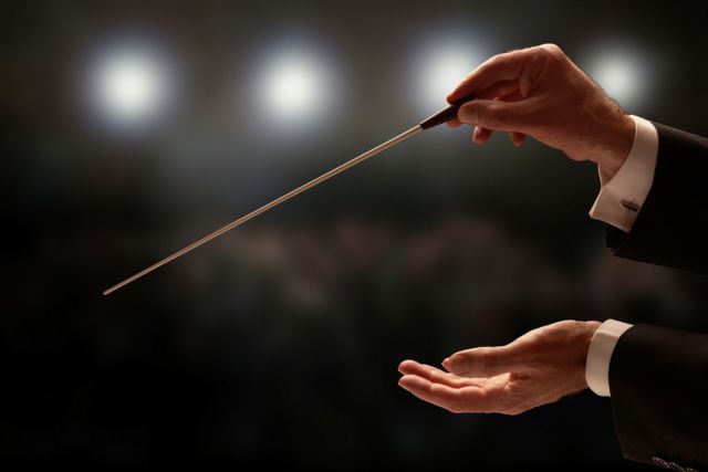 Conductor,Conducting,An,Orchestra,With,Audience,In,Background