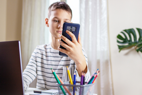 Kid,Sitting,With,Computer,And,Scrolling,Phone,Instead,Of,Doing