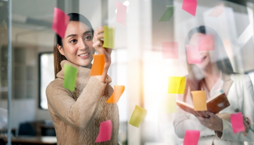Young,Businesswoman,Creative,Team,Using,Post,It,Notes,In,Glass